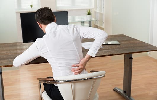Young Businessman Sitting On Chair And Suffering From Backache At Desk